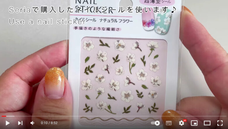 UVレジンアクセサリーに使用する花柄ネイルシールを手に持っている様子とSeriaで購入したネイルシールを使いますの字幕