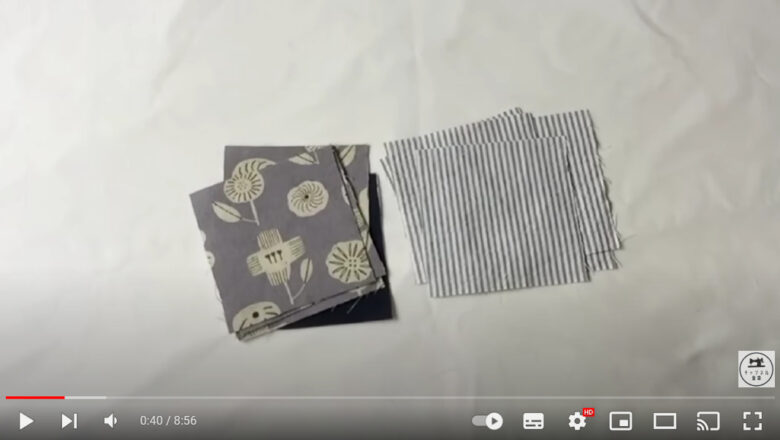 白い布の上に2種類の小さな布が置かれている画像。右は薄いグレーのストライプ柄、左は濃いグレーでヒマワリのような花柄をしている。