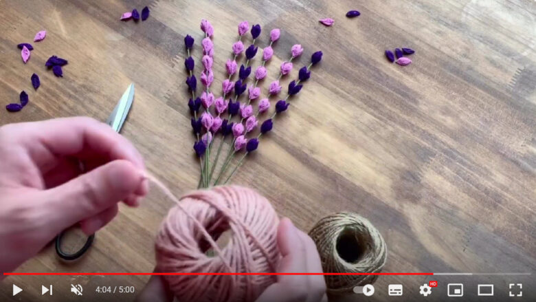 濃い紫色と薄い紫のちりめん生地でできたそれぞれのラベンダーをひもでまとめて花束を作っている様子